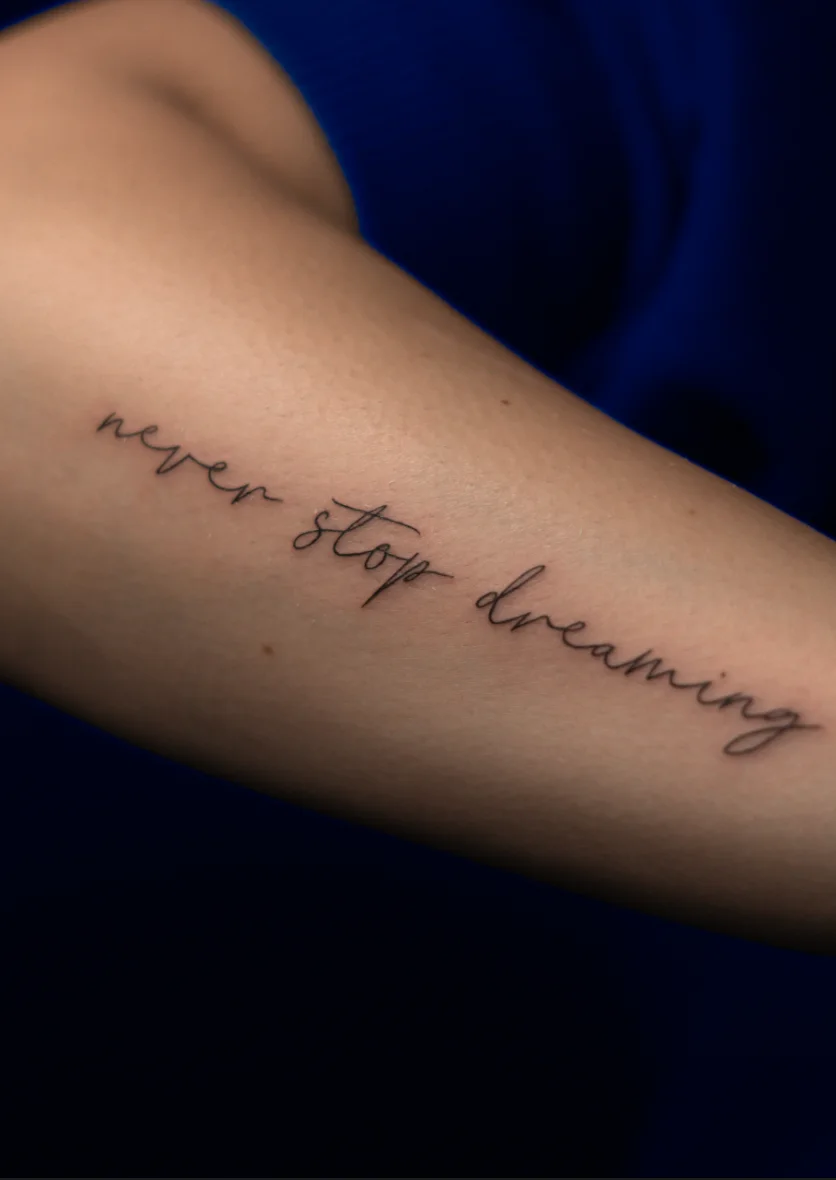 Odręczny napis never stop dreaming na przedramieniu